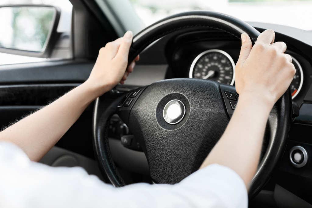 Kuljettajan kädet ohjauspyörällä auton sisätiloissa, mittaristo näkyy taustalla.