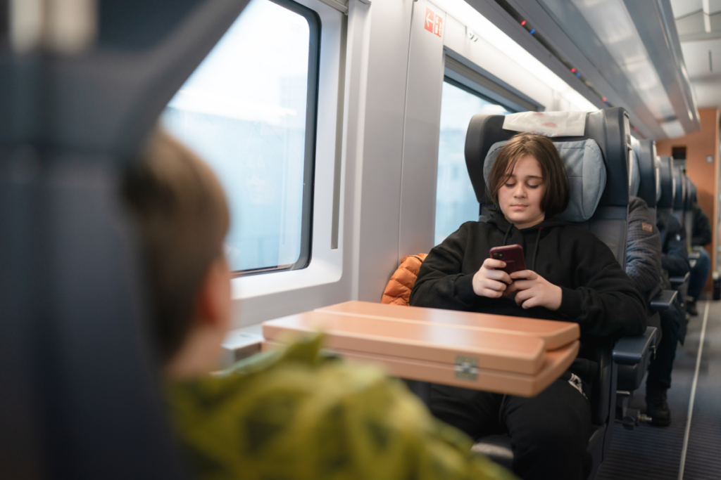 Lapsi istuu junan penkillä ja katsoo puhelinta pöydän ääressä matkustamon sisällä.
