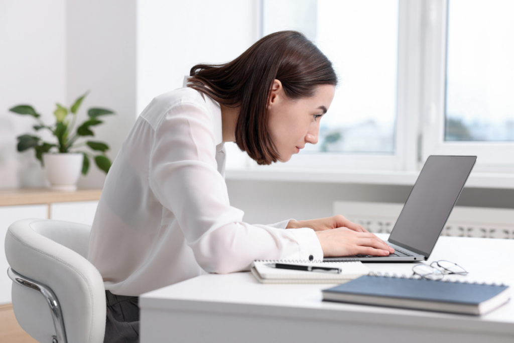 Aikuinen henkilö istuu työpöydän ääressä ja kirjoittaa kannettavalla tietokoneella ikkunan edessä