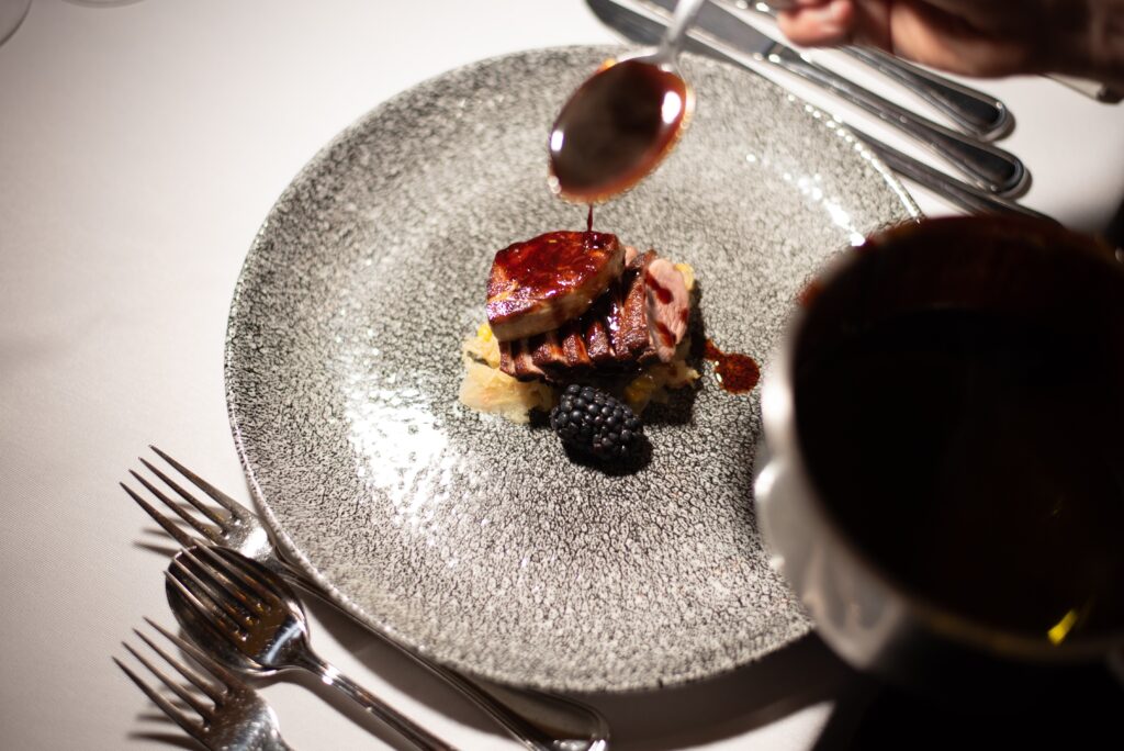 Ravintola-annos, jossa kastiketta kaadetaan lusikalla paistetun lihan päälle lautasella.