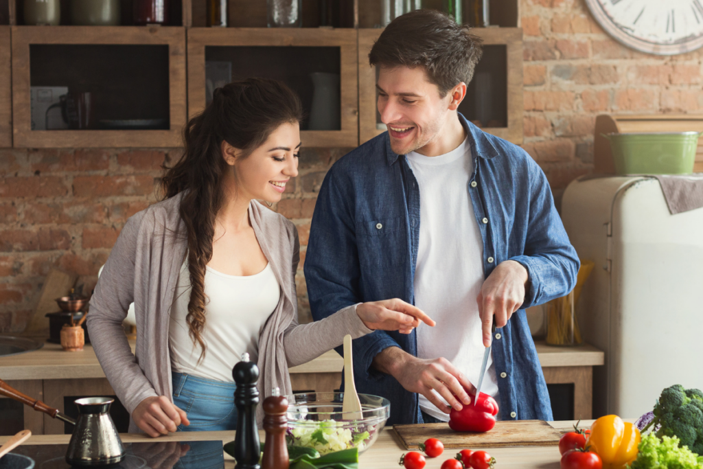 Pariskunta valmistaa ruokaa yhdessä keittiössä ja pilkkoo vihanneksia.