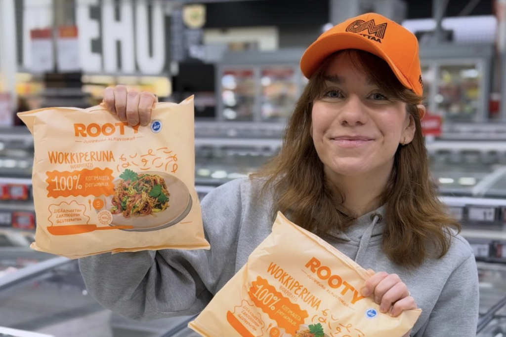 Henkilö seisoo kaupan pakastealtaan edessä ja pitelee käsissään kahta juurespohjaista pakasteperunatuotetta.