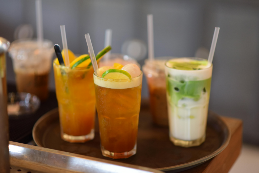 Tarjottimella useita kylmiä juomia laseissa: jääteetä sitruuna- ja limelohkoilla sekä vihreä matcha-juoma jääpaloilla ja pillillä.