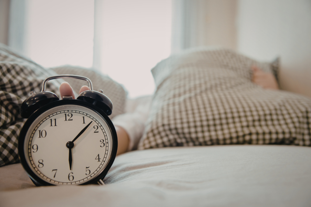 Kuva makuuhuoneesta. Etualalla herätyskello ja takana petaamaton sänky.