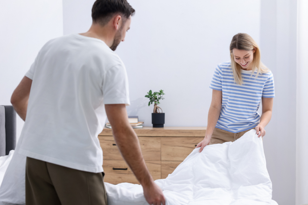 Pariskunta petaamassa sänkyä yhdessä makuuhuoneessa.