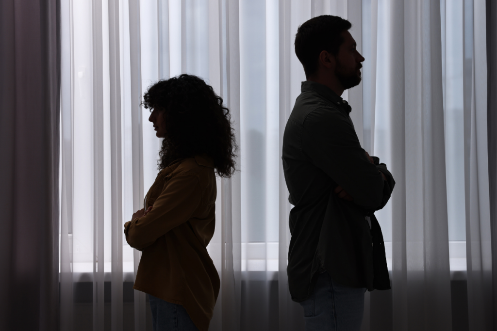 Mies ja nainen seisovat selät vastakkain kädet puuskassa ikkunan edessä.