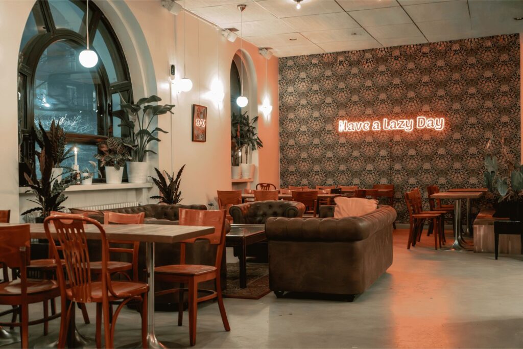 Tyylikäs ja rauhallinen kahvila-ravintolan sisätila, jossa puisia pöytiä ja tuoleja, nahkasohvia, viherkasveja sekä seinällä neonvalo, jossa lukee ”Have a Lazy Day”.