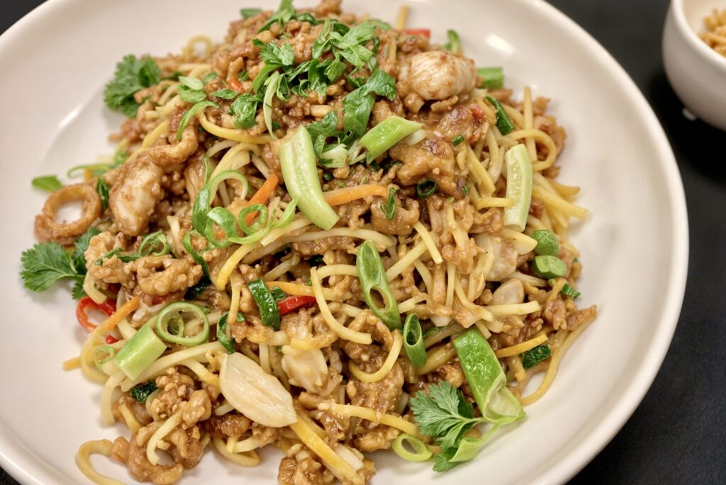 Kulhollinen wokkiperunaa, jossa on kanaa, kasviksia, kevätsipulia ja yrttejä.